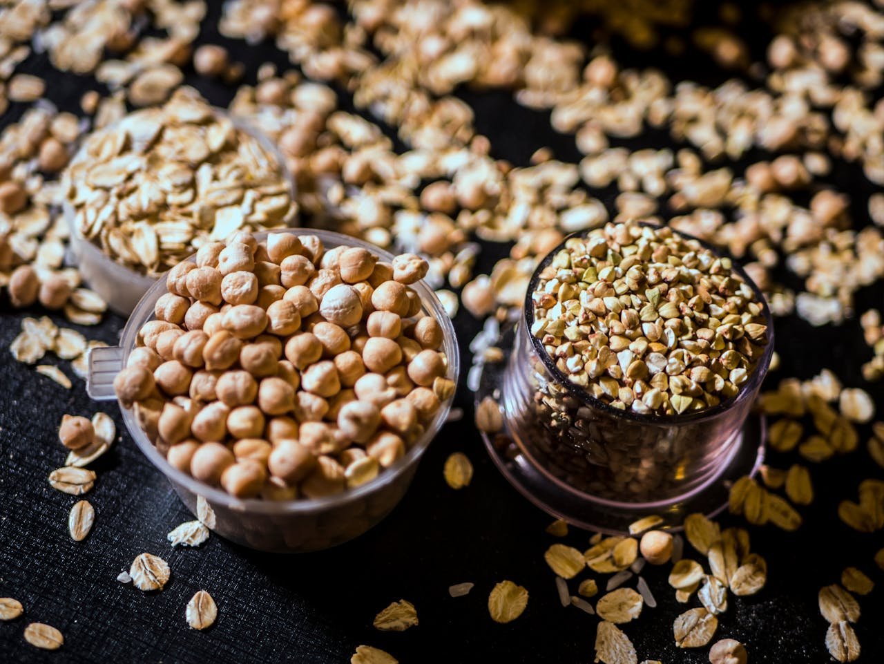 brand-03 Close-up of assorted raw grains and seeds in cups on a dark background, showcasing variety and texture.